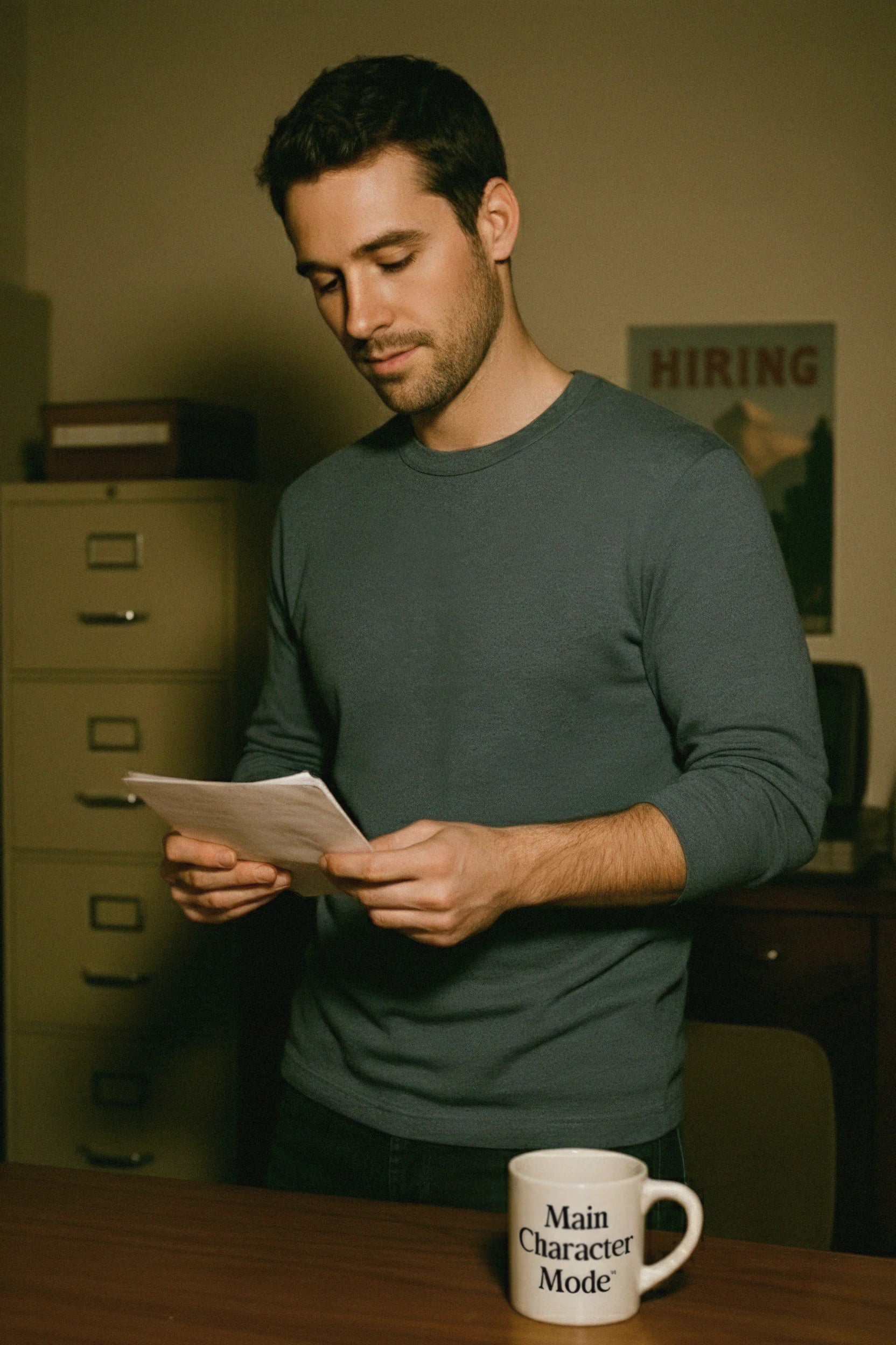 Man reading a piece of paper in an office setting with a mug on the table.