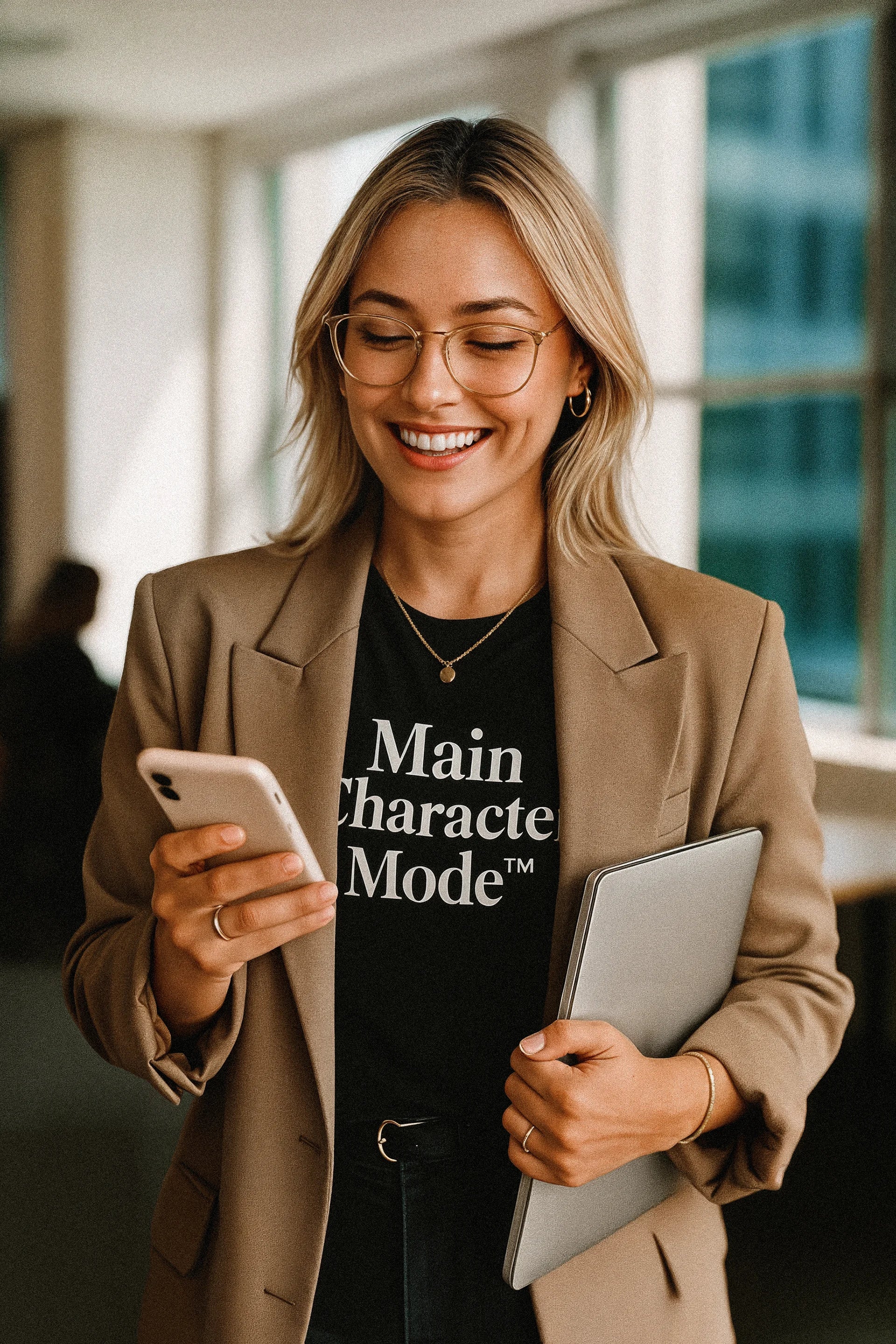 Woman holding a phone and tablet, wearing a 'Main Character Mode' shirt, in an office setting.